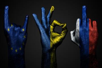 a set of three hands with a painted flag of Ukraine, Russia and the European Union show middle finger, goat and Okay, a sign of aggression, protest and approval on a dark background.