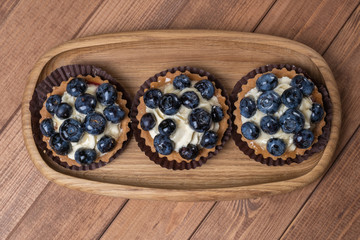 Obraz na płótnie Canvas three bilberry tartlet on a wooden plate on the table, bilberry baked shells, fruit cupcake with blueberry