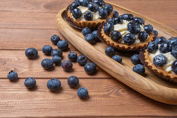 three bilberry tartlet on a wooden plate on the table, bilberry baked shells, fruit cupcake with...