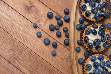 three bilberry tartlet on a wooden plate on the table, bilberry baked shells, fruit cupcake with blueberry