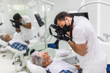 Handsome dentist making shots of mature patient's smile after treatment. Special camera with flash ring shadowless.