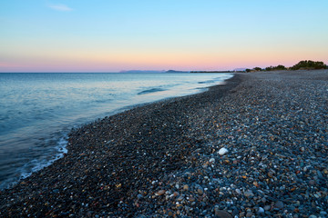 The sunset on the pebble beach with hills on the background, Kolymbari, Crete, Greece.