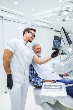 Portrait of handsome smiling dentist looking at x-ray image of his patient.