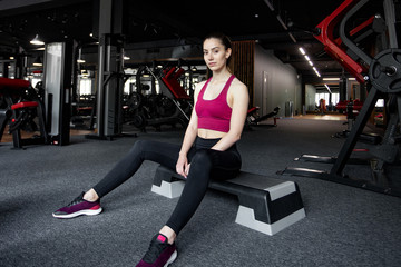 Fototapeta na wymiar Close up portrait of young pretty european fitness woman sitting on the step platform at the gym. Breaking relax while exercise workout. Concept of health and sport lifestyle. Athletic Body.