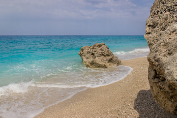 Beach with cyan blue water and rock with blue sky in the background