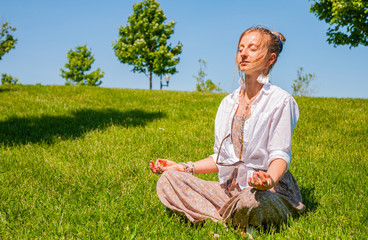 Happy woman is meditating sitting in Lotus pose on grass lawn. Beautiful boho style woman with...