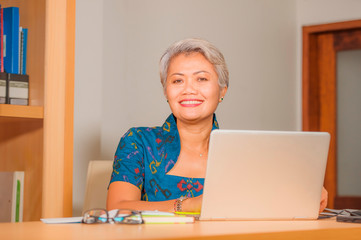 Fototapeta na wymiar Lifestyle portrait of Happy and attractive elegant middle aged Asian business woman working smiling at office computer desk feeling positive and successful