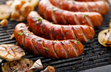 Grilling sausages with the addition of herbs and vegetables on the grill plate, close-up. Grilling...