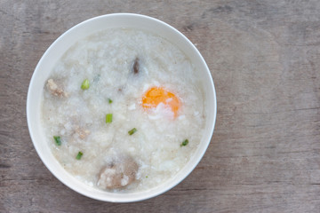 Rice porridge or congee with egg in white bowl on vintage wooden table background.