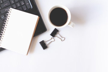 Notebook with laptop, paper clip and cup of coffee on white background. Flat lay top view.