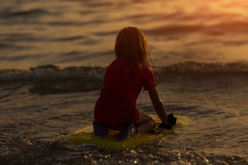 Happy Surfing girl on a beach looking on the sea and ready to go into the water. Sunset time