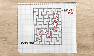 Problem Solving maze, Problem Solved text, maze solution hand drawn on with red marker on graph paper over wooden desk from problem to solution, horizontal view