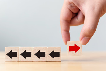 Hand holding wooden block with red arrow facing the opposite direction black arrows, Unique, think...