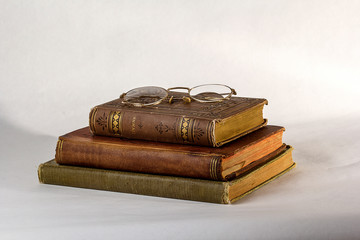 Stack of Three Antique books with a pair of vintage eyeglasses on a white background.