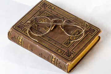 A pair of Antique Eyeglasses sitting on a vintage hymnal on a white background.