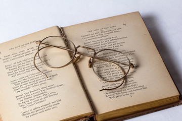 A pair of Antique Eyeglasses sitting on a opened vintage hymnal on a white background.