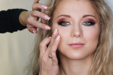 Fototapeta premium Make-up artist working in make-up studio, applying makeup on face of female clients. Makeup artist emphasizes cheekbones. Evening make-up.