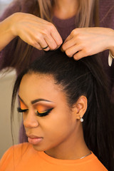 Young woman African American with perfect skin and radiant make-up in orange-coloured shades makes laying at the hairstylist in the beauty salon. Desire to be beautiful. Close-up