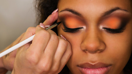 Obraz premium Makeup artist draws arrows on eyelids of african girl. Evening make-up.