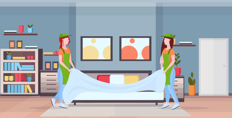 couple chambermaids changing the bedding or bedclothes girls in uniform working together cleaning service concept modern bedroom interior flat full length horizontal