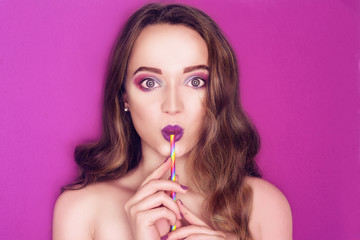 Fashion model woman creative colorful pink and blue make up. Beautiful cute girl Purple bright lips, long cerly hair. Model drinking a cocktail of paper straws. Caring for nature. Purple background.