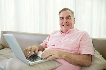 Happy senior man enjoyng playing game on laptop at home