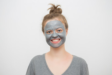 Young caucasian woman with black or grey facial clay mask on her face, smiling