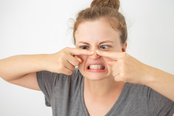 Young caucasian woman squeezing a pimple on her nose, funny facial expression