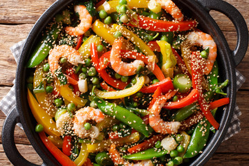 Roasted shrimps with peppers, onions, herbs, pod peas, sesame close-up in a frying pan. horizontal top view