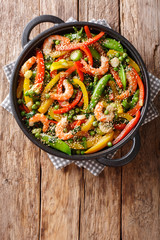 Vegetable stir fry with shrimps and sesame close-up in a frying pan. Vertical top view