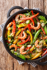 Stir-Fried shrimp with vegetables, sesame close-up in a pan on the table. Vertical top view
