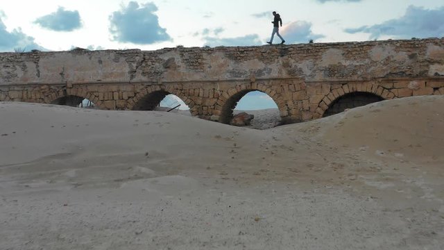 Aerial: Man Running on Stone Bridge on a Beach in Caesarea, Israel