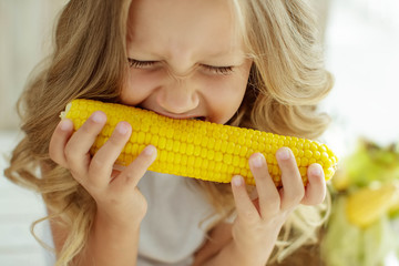 Child with vegetables. Girl holding corn in the hands.