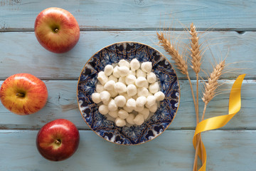Symbols of jewish holiday - Shavuot. Top view of mozzarella, ears of wheat and red apple on a blue wooden background.