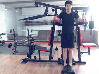 Fit young Asian man exercising with machine at sport gym. Fitness and workout concept