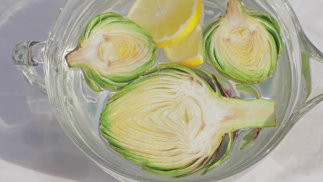 look from above on lemon slices and artichoke floation in the glass bowl with water