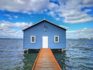 Blue boat house with a wooden pier leading to the front door. The Crawley Edge