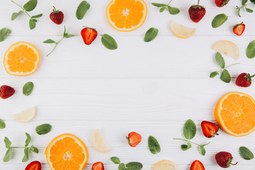 Summer colorful flat lay. Pattern made of citrus fruits, leaves and strawberries on the white wooden table. Top view and copy space