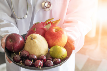 Doctor or nutritionist hold bowl of fresh fruits of apples, orange, cherry, nashi pear, and dragon fruit with copyspace. Medical healthcare nutrition concept.