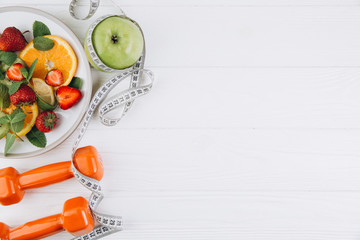 Diet plan, menu or program, tape measure, water, dumbbells and diet food of fresh fruits on white...