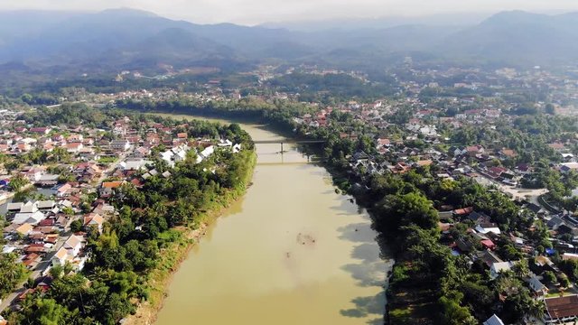 Aerial view of Luang Prabang and surrounding lush mountains of Laos. The Nam Kahn River, a tributary of the Mekong River, flows peacefully on the right.