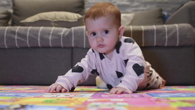 beautiful little girl with red hair who plays and tries to stand up, first steps