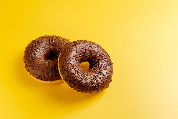 two chocolate donuts on yellow background top view