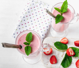 Glass of fresh strawberry and yogurt smoothie on white wooden table.