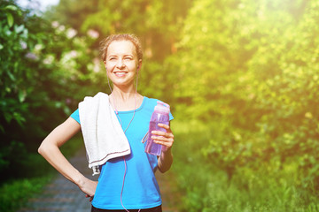 Fitness woman with bottle and towel of water after running training in summer park