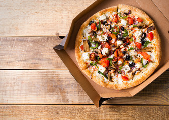 Delivery concept. Vegetable pizza in open cardboard box on wooden table