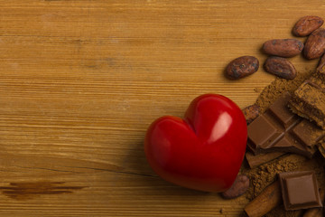 Cocoa beans, chocolate, cocoa powder, heart and cinnamon on wooden background