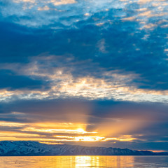 Square frame Golden sun shining through the cloudy sky and reflected on the shiny lake below