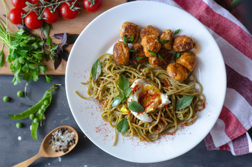 Spinach spaghetti with meatballs and egg. Green tasty pasta served with cherry tomatoes and basil