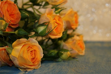   beautiful yellow roses with buds and green leaves lie on blue wooden boards on a shiny background